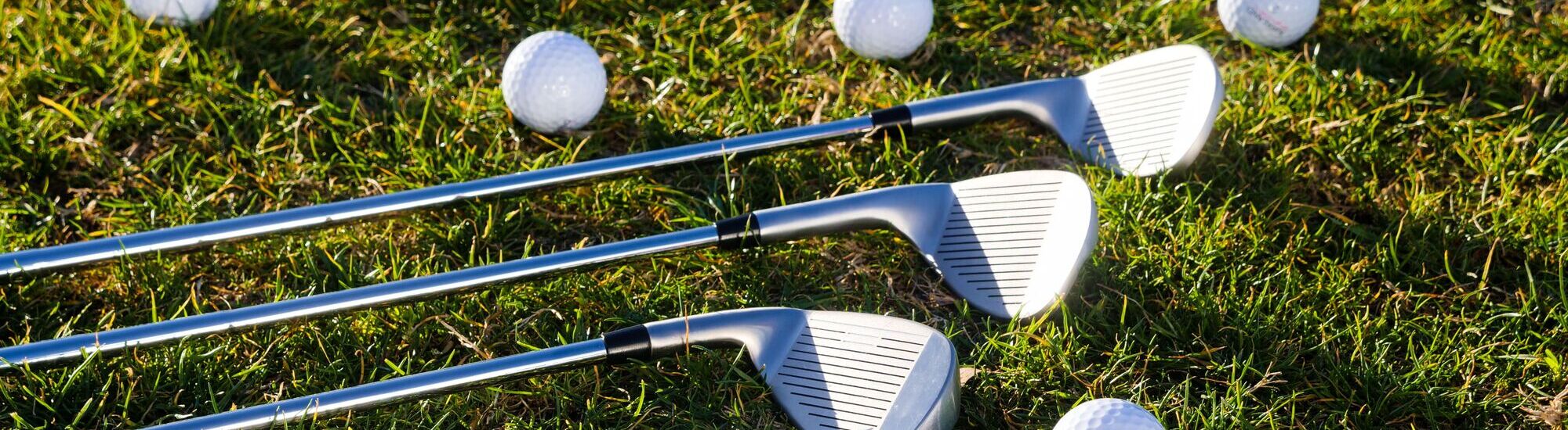 Three golf clubs resting on grass with several golf balls scattered around.